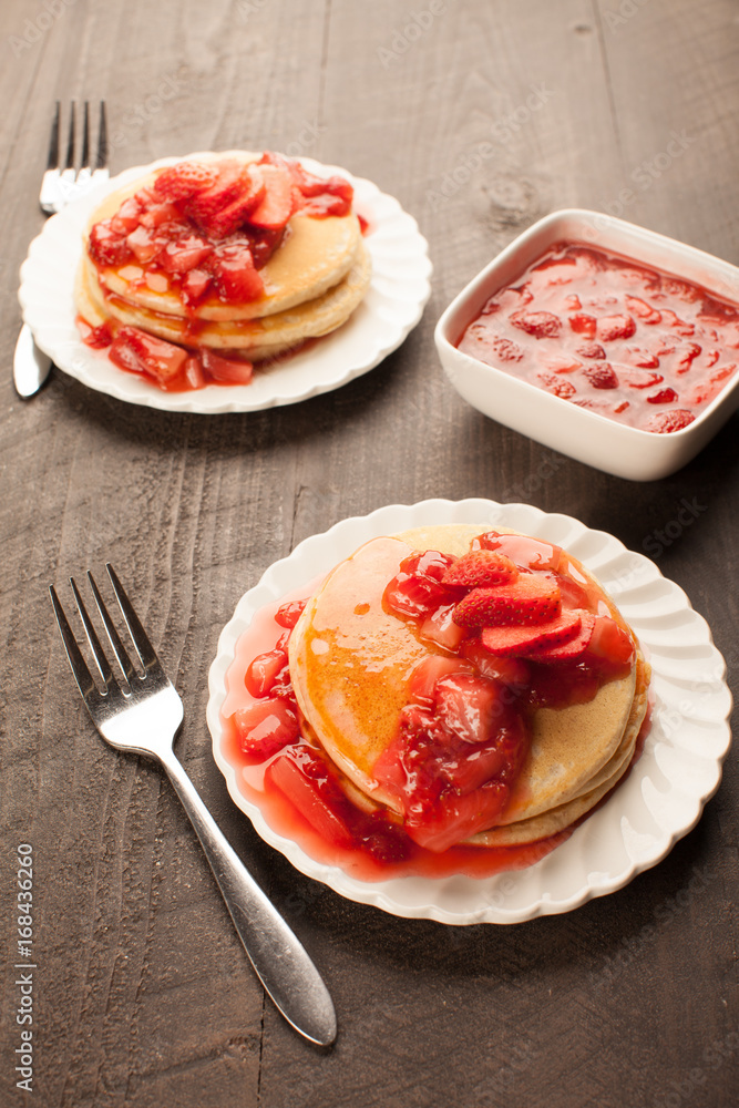 Freshly made white flour pancakes stacked on white plates topped with red strawberry syrup vertical shot
Freshly made white flour pancakes stacked on white plates topped with red strawberry syrup vertical shot