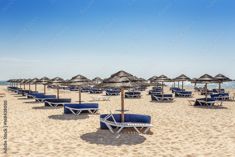 Beach zone for sunbathing with umbrellas and sun loungers. Portugal.
