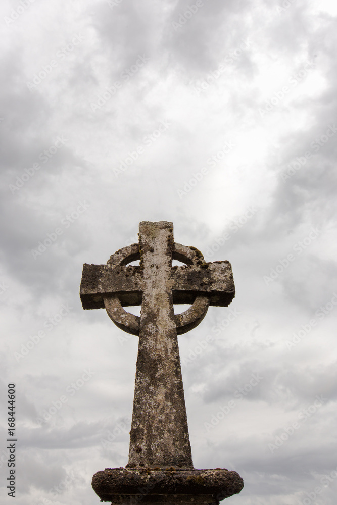 A celtic cross in an Irish cemetery against a cloudy sky