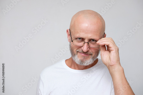 adult bearded bold grizzled man in eyeglasses looking with grain of salt (skeptically) or inquiringly isolated on gray photo