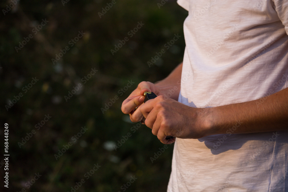 Caucasian guy in a white shirt changing replacing filling bullets in magazine of the  pistol in the nature ready to start shooting in the target aiming