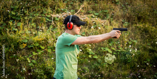 Profile of a brunette professional policeman killer special army forces training outside in the wilderness to fight criminals aiming at the enemy target with his gun  pistol shooting bullets