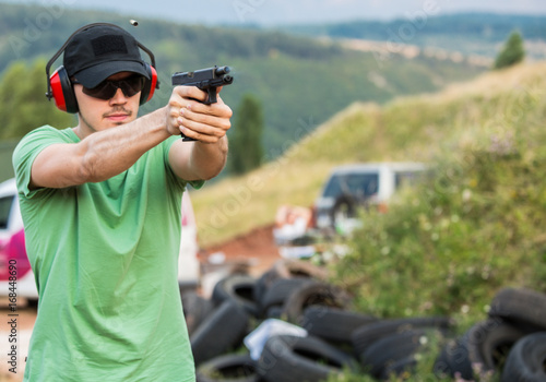 Handsome young guy aiming with the pistol at the distant target on the training field for special army and police forces in the outside field shooting with fire arms gun  pistol bullet in the air