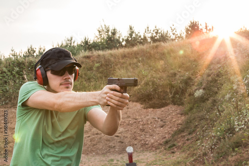 Outside training of the young and handsome muscular caucasian policeman or special force army soldier shooting bullets with gun pistol from firearms at the criminal enemy target in the nature