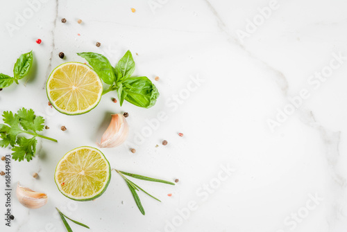 Food cooking background, white marble kitchen table. Spices and herbs for cooking dinner - coriander, parsley, basil, rosemary, lime, tomato, salt, pepper, garlic. Copy space top view