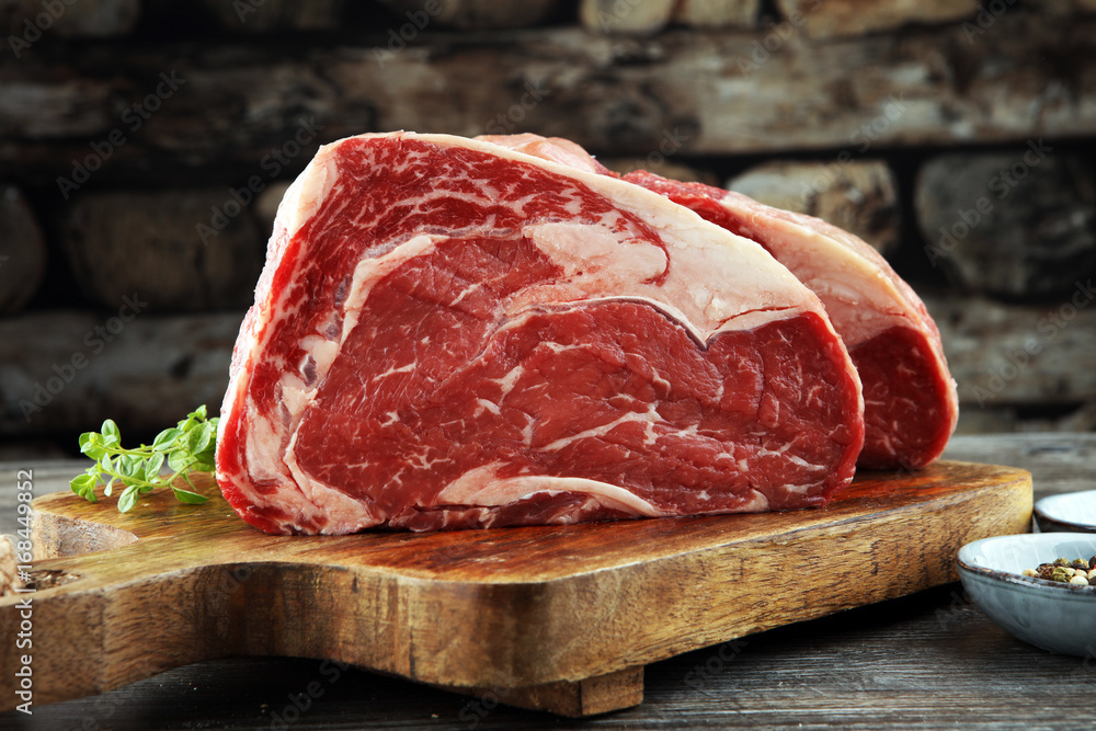 Raw fresh meat Ribeye Steak, seasoning and meat fork on dark background - obrazy, fototapety, plakaty 