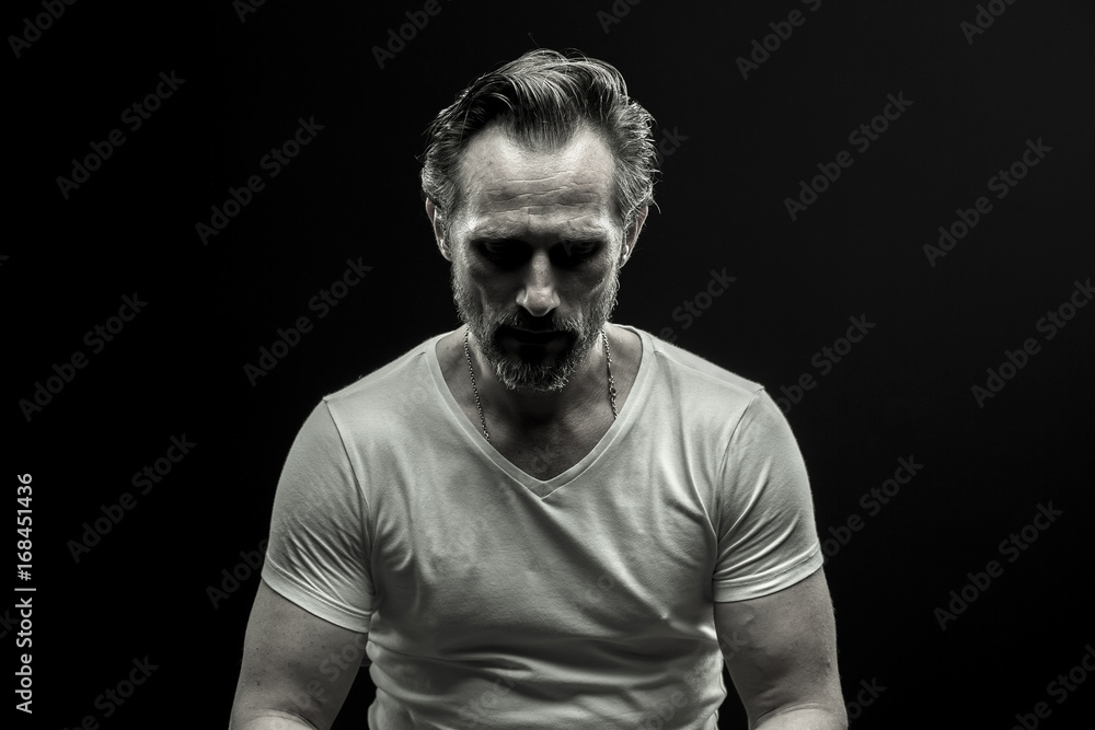 Black and white portrait of mid aged man. Male in white t-shirt on black background showing emotion of disappoinment.