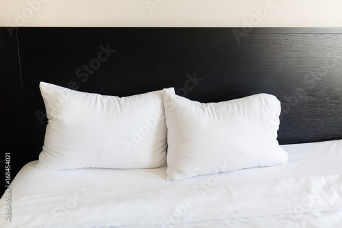 White pillows on the beds made with a black back. Bed made up with clean white pillows and bed sheets in room. Close-up.