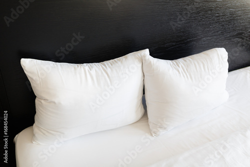 White pillows on the beds made with a black back. Bed made up with clean white pillows and bed sheets in room. Close-up.
