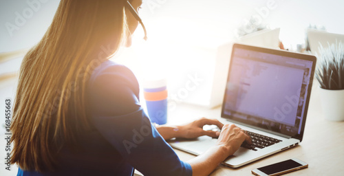 Bilde på lerret Portrait of beautiful business woman working at her desk with headset and laptop