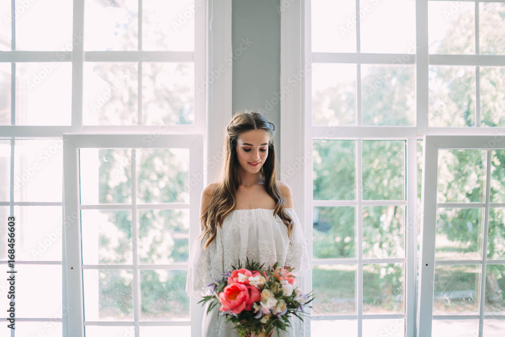 Bride holds in hands a rustic wedding bouquet with white roses and crimson peonies on window background. Close-up Bride holds in hands a rustic wedding bouquet with white roses and crimson peonies on window background. Close-up