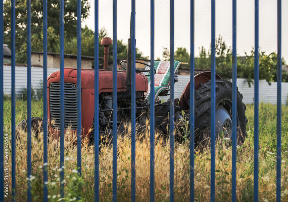 Fototapeta premium Red old tractor behind a blue fence