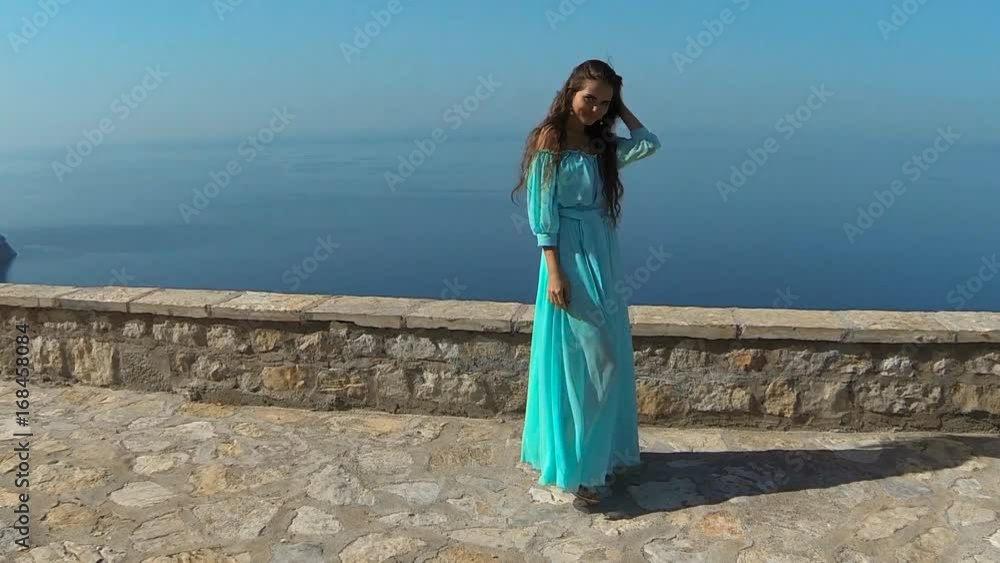 Beautiful brunette smiling Girl with Healthy Long Hair in blowing dress. Happy Young Woman Enjoying Nature and having Fun over sea and blue sky. Sveti Stefan, Montenegro. Beautiful brunette smiling Girl with Healthy Long Hair in blowing dress. Happy Young Woman Enjoying Nature and having Fun over sea and blue sky. Sveti Stefan, Montenegro.