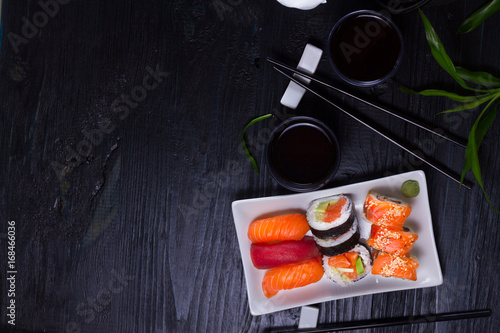 Fotografie Japanese sushi dish with tea and chopsticks on black wooden background with copy