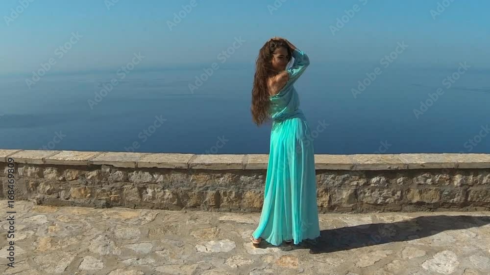 Beautiful brunette smiling Girl with Healthy Long Hair in blowing dress. Happy Young Woman Enjoying Nature and having Fun over sea and blue sky. Sveti Stefan, Montenegro. Beautiful brunette smiling Girl with Healthy Long Hair in blowing dress. Happy Young Woman Enjoying Nature and having Fun over sea and blue sky. Sveti Stefan, Montenegro.