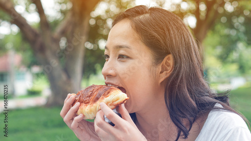 Asian woman holding and eating fresh baked bakery in green background park