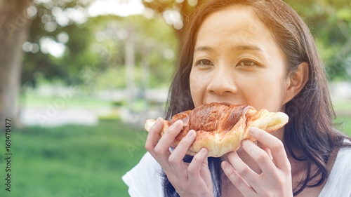 Asian woman holding and eating fresh baked bakery in green background park