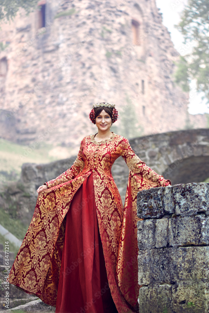 Beautiful Isabella of France, queen of England on Middle Ages period in red gown near medieval castle Beautiful Isabella of France, queen of England on Middle Ages period in red gown near medieval castle