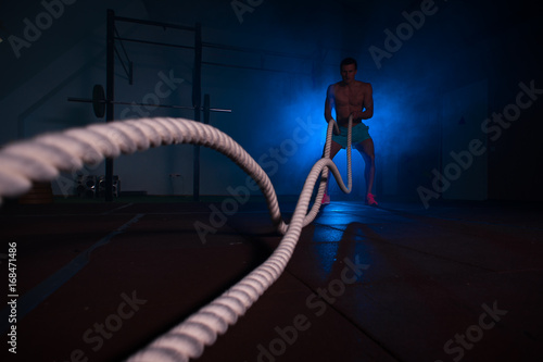 Muscular fitness man exercising with battle ropes