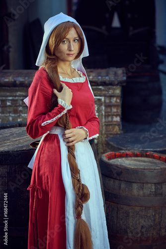 Townswoman in red dress with an apron and chaperone on the street. Costume stylized of later Middle Ages on 15/ 16th century. photo