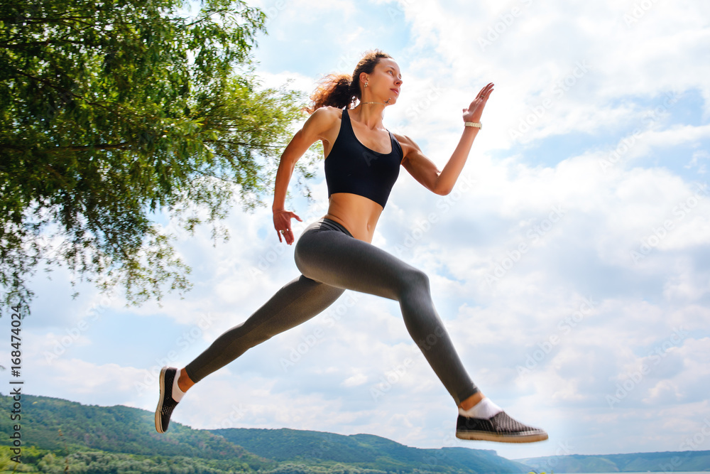 Fototapeta premium A beautiful sporty woman runing on the shore of a lake in sportswear. Girl is exercising
