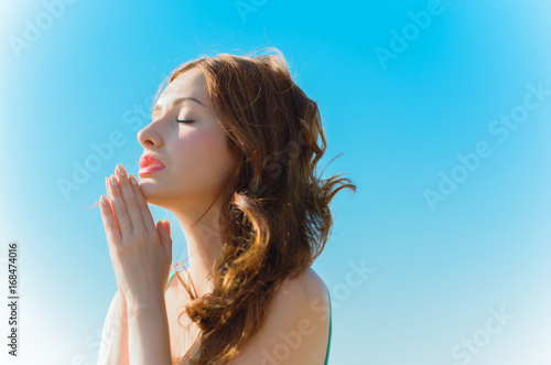 Closeup portrait of a young woman praying. Pray in the Morning , Woman praying with hands together on blue background. Believers meditates in the cathedral. Spiritual time of prayer.