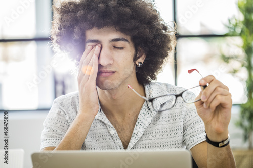 Young man working with computer while rubbing his eye photo