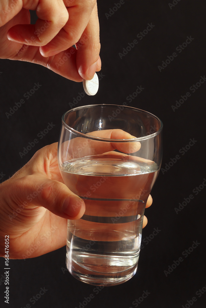 Hand with a soluble pill from headache over the glass of water on a black background. Hand with a soluble pill from headache over the glass of water on a black background.