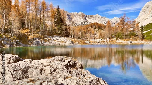 Mountain hut by Alpine lake in autumn season. Pan right, UHD.