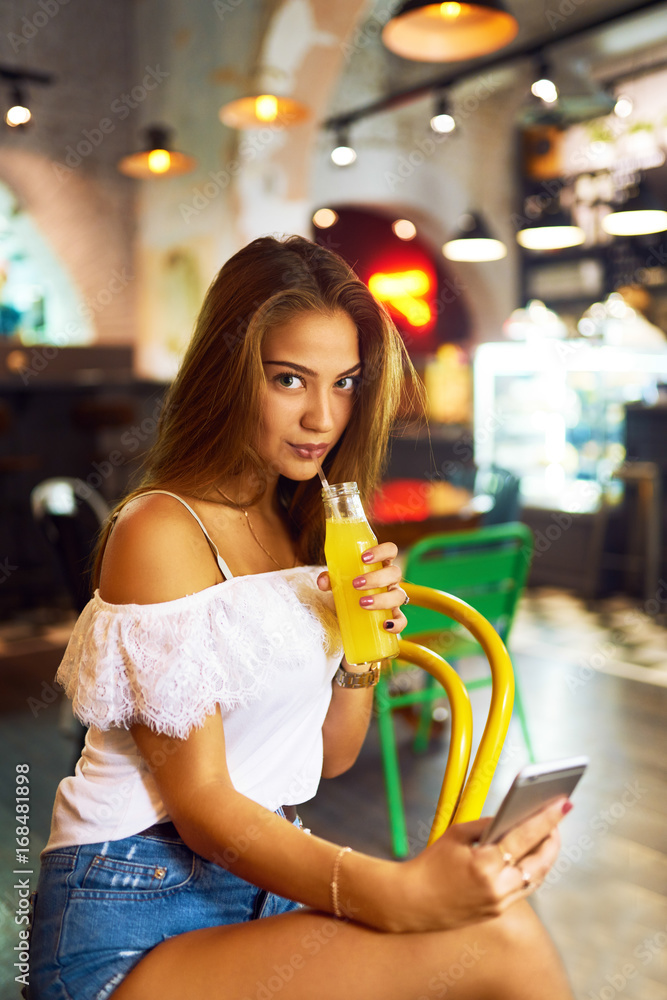 Young, beautiful girl with a lovely smile sitting in a cafe drinking lemonade and using a phone. Excellent summer mood. Background blur
Young, beautiful girl with a lovely smile sitting in a cafe drinking lemonade and using a phone. Excellent summer mood. Background blur