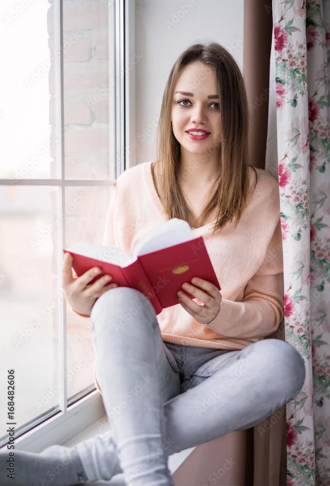 Young woman sitting at window reading a book