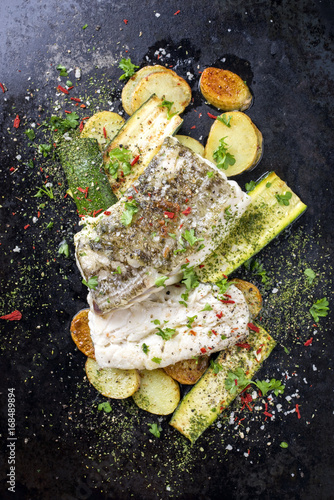 Fried cod fish fillet with vegetable and potatoes as top-view on old metal sheet