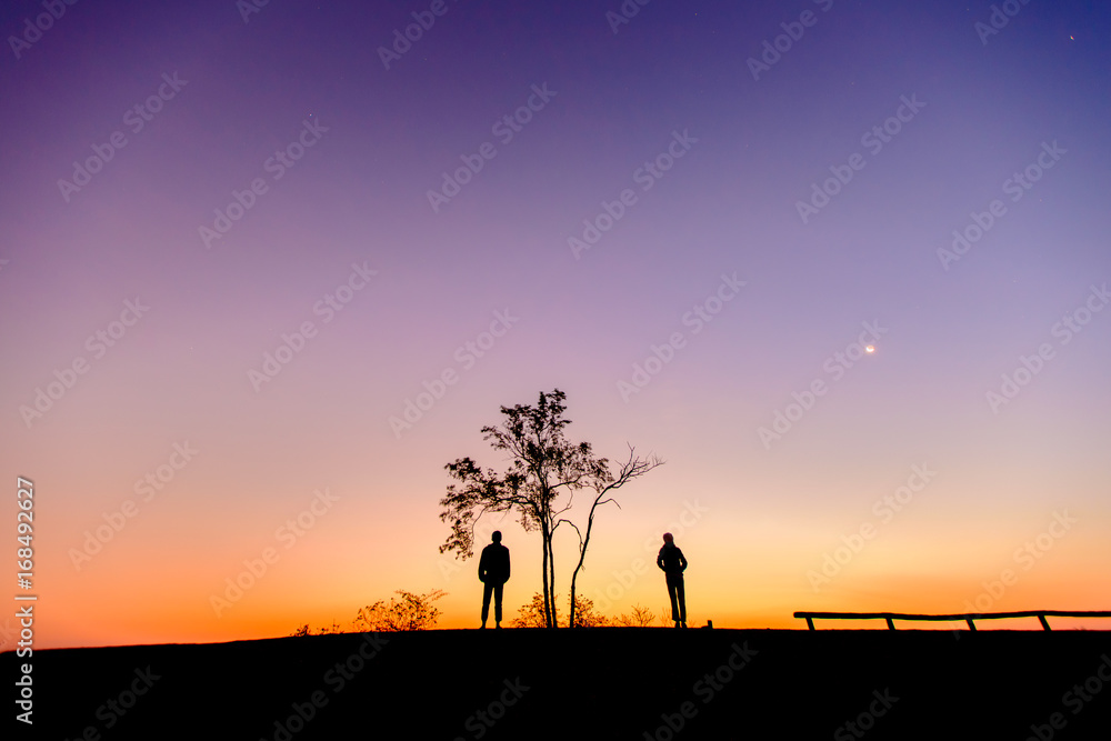 Silhouette of a couple watching beautiful sunrise on the mountain.  beautiful dawn light with copy space. Romantic love concept.