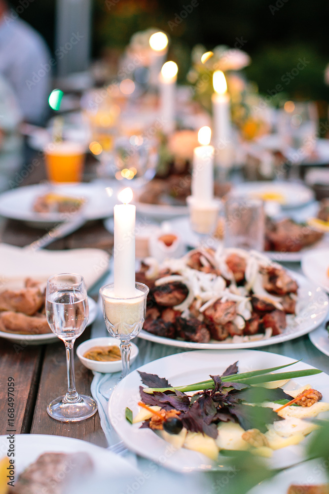 comfort, food, setting concept. dining table for celebrating holidays in the wild, there is silverware, dishes full of delicious meal, glasses with water and candles for cosy atmosphere