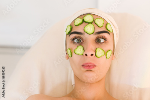 Girl grimaces with a cucumber mask on her face