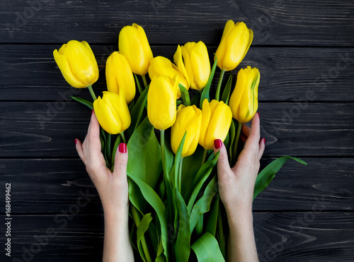 Female hands holding yellow tulips on black vintage wooden table. Flat lay, top view #168499462