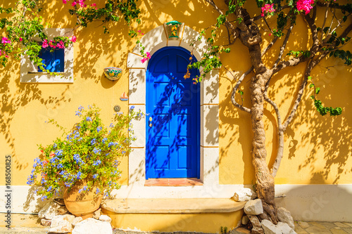 Wallpaper Mural Blue door of a yellow Greek house decorated with flowers, Assos town, Kefalonia