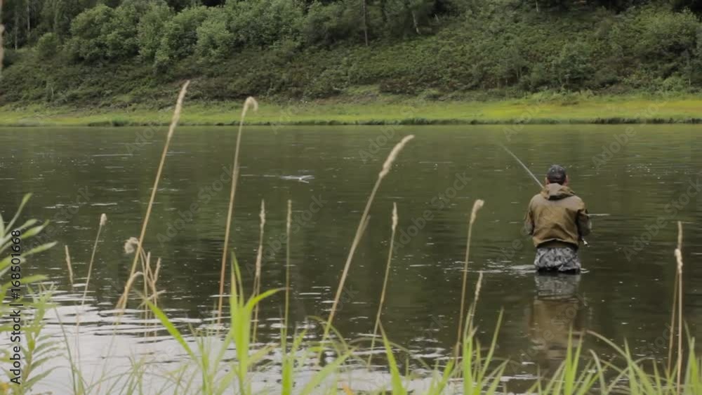 Joyful fisherman is fishing in calm river water near the shore Joyful fisherman is fishing in calm river water near the shore