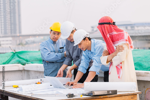 Arabian businessman and Engineer and Laborer working and discussion with laptop  on construction plans front of building in his work site. Teamwork concept