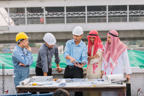 Two Arabian businessman and Engineer and Laborer working and discussion with laptop on construction plans front of building in his work site. Teamwork concept