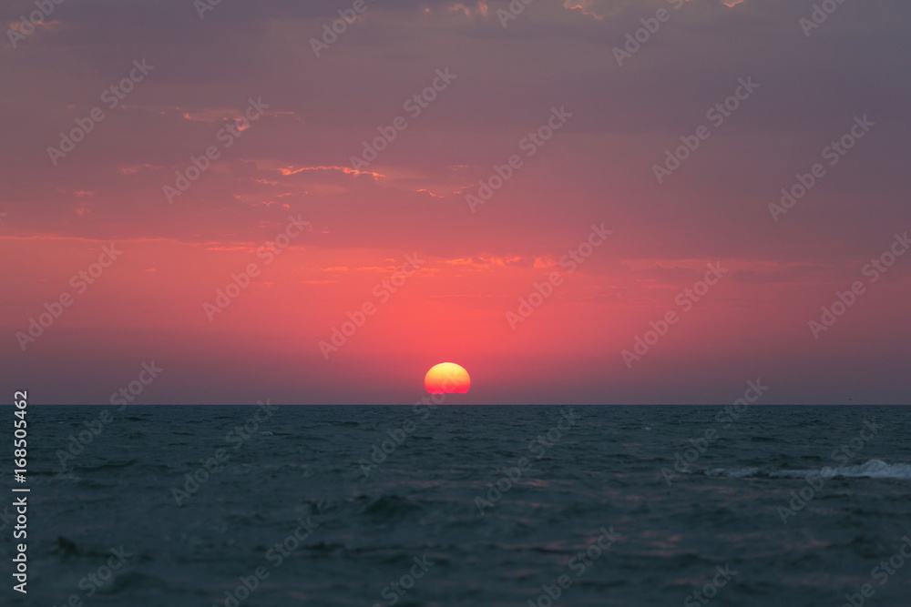 Dawn over the sea, the red sun rises above the horizon
