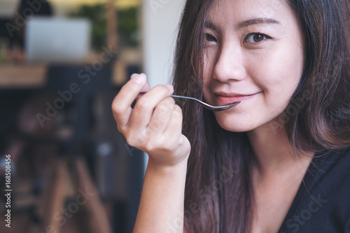 Closeup image of an Asian woman with smiley face eating food by spoon in modern cafe
