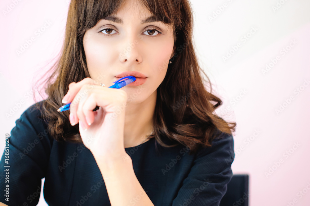Portrait of a beautiful business woman making notes in a notebook. Holds a pen, sitting in the workplace in a pink office Portrait of a beautiful business woman making notes in a notebook. Holds a pen, sitting in the workplace in a pink office