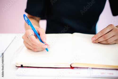 Business woman making notes in notepad. Beautiful well-groomed hands close-up hands, holding a pen, sitting in the workplace