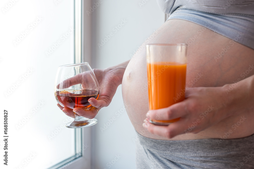 Pregnant woman belly holding alcohol and juice in hands. Concept choice for a healthy lifestyle during pregnancy Pregnant woman belly holding alcohol and juice in hands. Concept choice for a healthy lifestyle during pregnancy