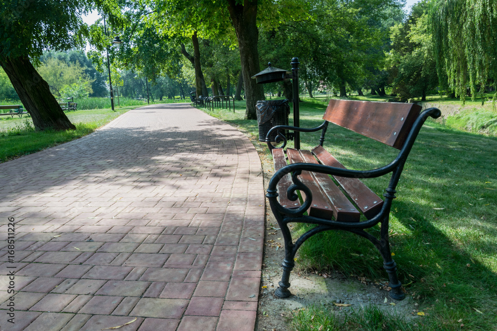 Wooden bench in a green park next to a foot path Wooden bench in a green park next to a foot path