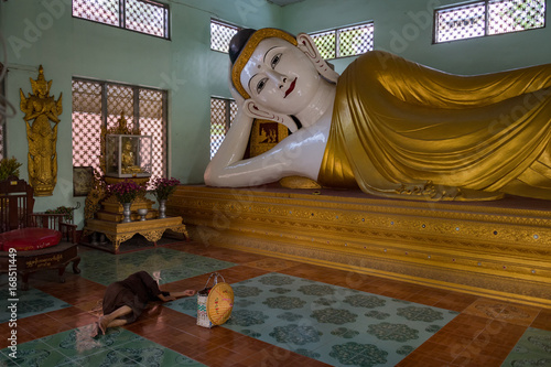 Woman sleeps alongside a Reclining Buddha in the Setyyanthiha Paya temple, Mandalay, Myanmar photo