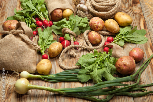 Fresh vegetables potatoes  radishes  onions  rope and bag on a wooden background