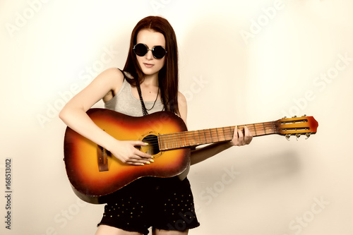 Young beautiful hippie playing guitar on light background