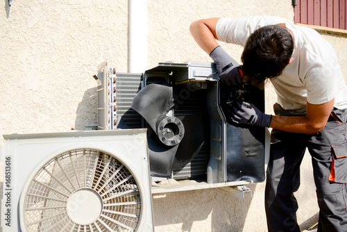 young man electrician installer working on outdoor compressor unit air conditioner at a client's home